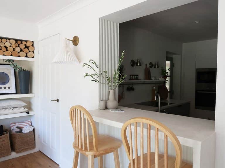 white concrete breakfast bar with wooden high-backed stools and built-in shelves in the background