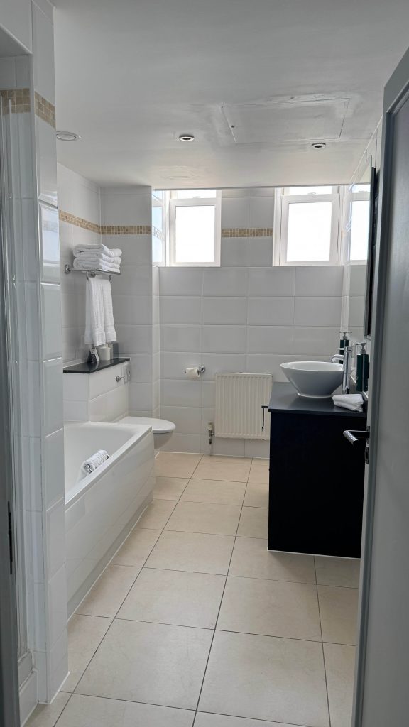 Bright bathroom featuring white tiled walls, a sleek black vanity, and a contemporary vessel sink. N.